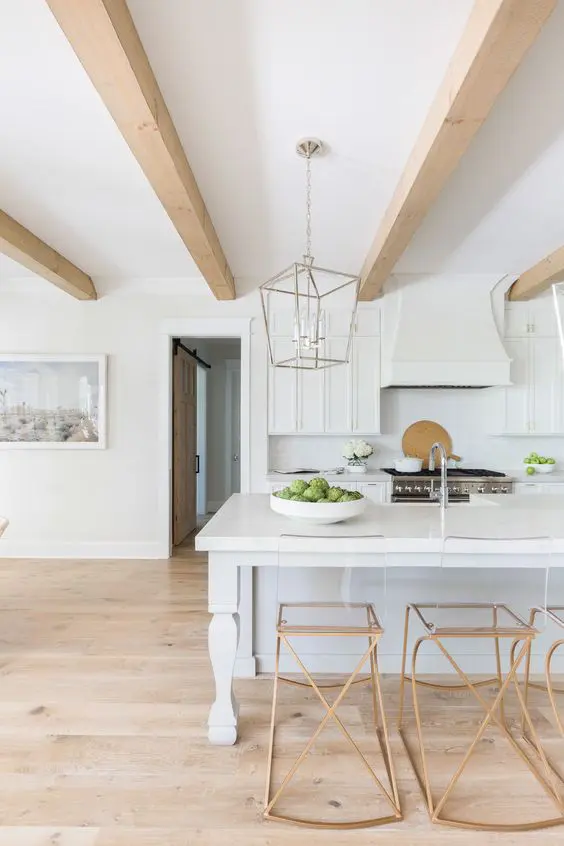 An airy white kitchen with an elegant kitchen island, copper stools, light colored wooden beams that add warmth to the space