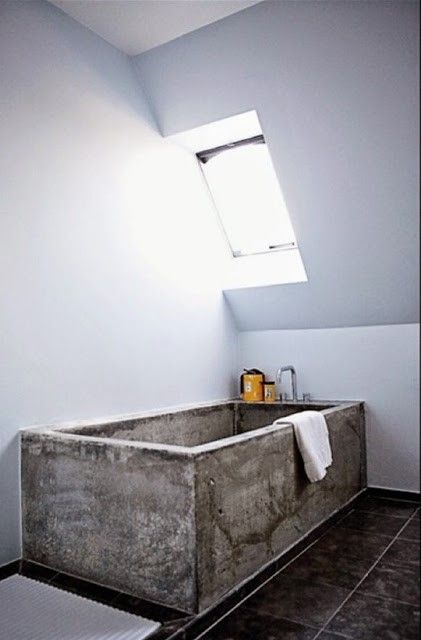 an attic bathroom with a concrete bathtub and black tiles on the floor is a gorgeous contemporary space that feels airy