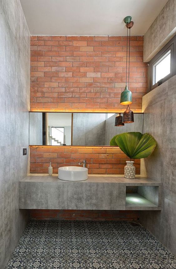 an industrial bathroom with concrete walls and a built-in vanity, a patterned tile floor, a brick wall and catchy pendant lamps