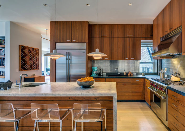 a rich-stained mid-century modern kitchen with a large kitchen island with a stone countertop and pendant lamps  (Above Construction)