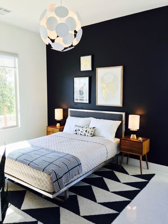 A bold and dramatic mid century modern bedroom with a blakc statement wall, a geometric rug, a black bed and rich stained nightstands