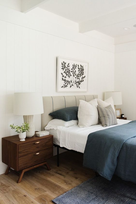 a bold mid-century modern bedroom with a grey leather bed, dark stained nightstands, navy rugs and bedding