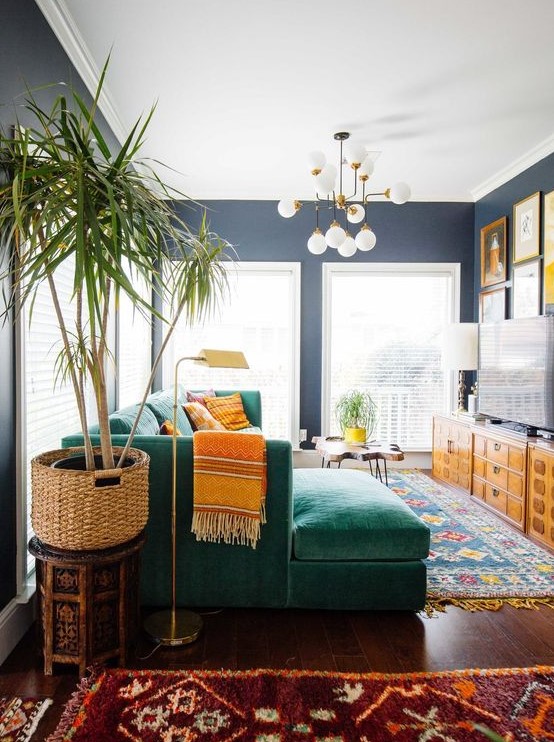 A bold mid century modern living room with colorful printed rugs, an emerald sectional, printed pillows, stained storage unit and a colorful gallery wall