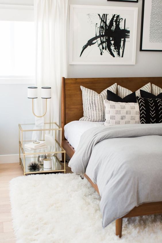 A bright mid century modern bedroom with a rich stained bed, a white fluffy rug, a gilded frame nightstand and an abstract artwork