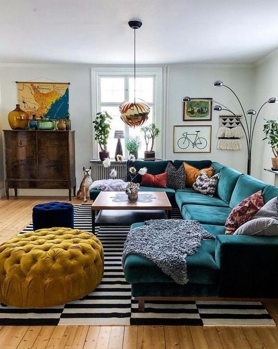 A bright mid century modern living room with a stained storage unit, a dark green sectional, a yellow ottoman and a navy pouf, colorful pillows and a bold gallery wall