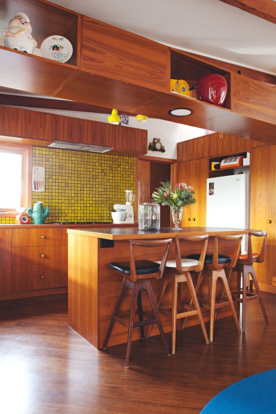 a bright mid-century modern kitchen with rich-stained cabinets, a yellow tile backsplash and tall wooden stools with backs