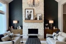 a chic living room wiер a black accent wall, a fireplace, grey sofas, black benches, a black ottoman and a vintage chandelier