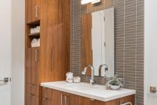 a chic mid-century modern bathroom with catchy grey tiles, stained wooden furniture, a mirror with a lamp over it