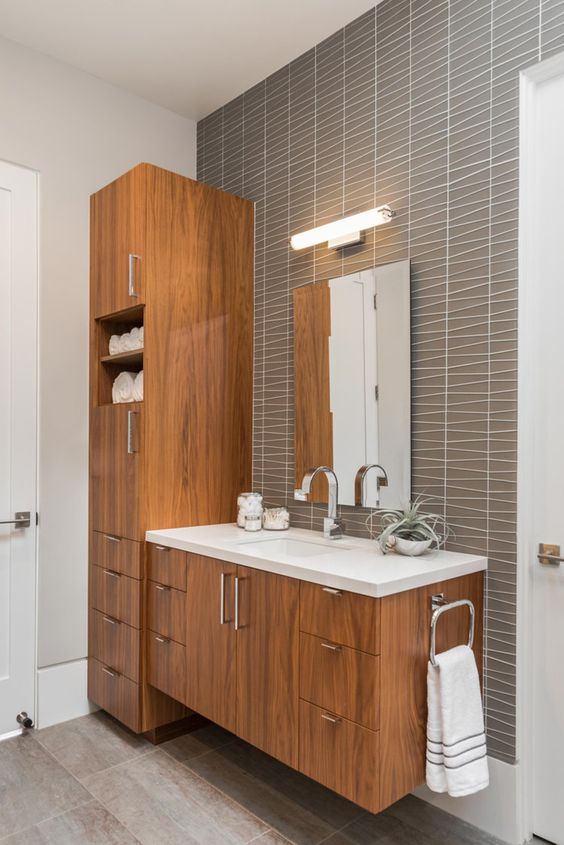 A chic mid century modern bathroom with catchy grey tiles, stained wooden furniture, a mirror with a lamp over it