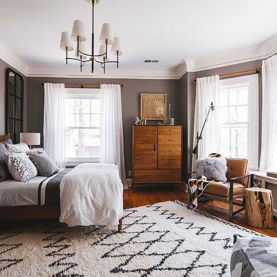 A chic mid century modern bedroom with a rich stained wooden dresser, a leather chair, a printed rug and a chic chandelier