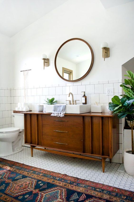 A classic mid century modern bathroom with white square and penny tiles, a boho rug, a wooden vanity and touches of brass
