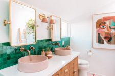 a colorful mid-century modern bathroom with green tiles for a backsplash, mosaic ones on the floor, pink sinks and lamps and a catchy wall art