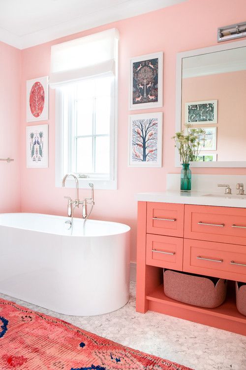 a colorful mid-century modern space with light pink walls, marble tiles, a coral vanity and a bright pink rug and a gallery wall