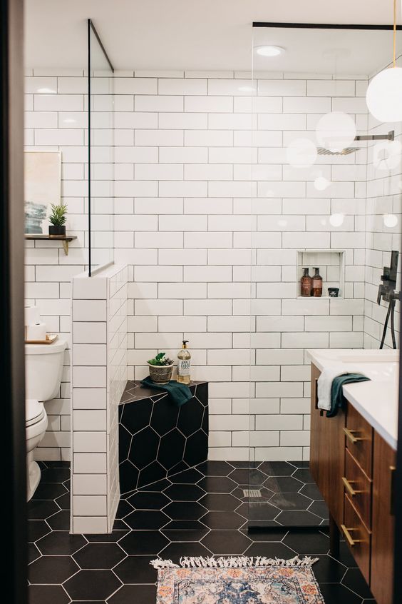 a contrasting mid-century modern bathroom with white subway and black hex tiles, a rich stained vanity and touches of gold