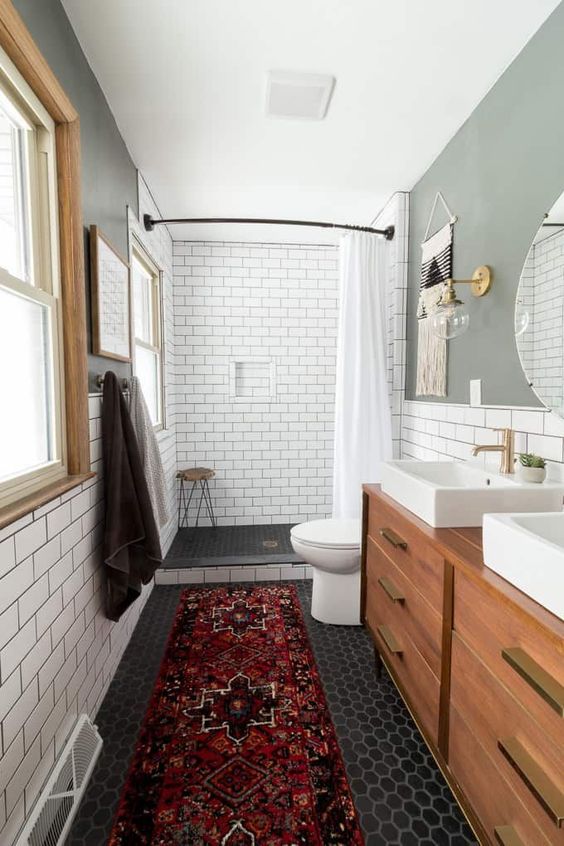 A cozy mid century modern bathroom with white subway and black hex tiles, with a wooden vanity, a boho rug and windows