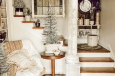 a cozy shabby chic entry with an upholstered chair, a wooden table, snowy trees in pots and a rug