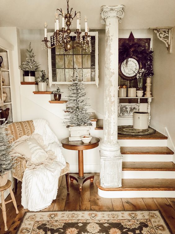 a cozy shabby chic entry with an upholstered chair, a wooden table, snowy trees in pots and a rug