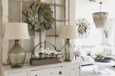 a cute shabby chic entryway with a chic sideboard, a wire basket, lamps, frames with a greenery wreath