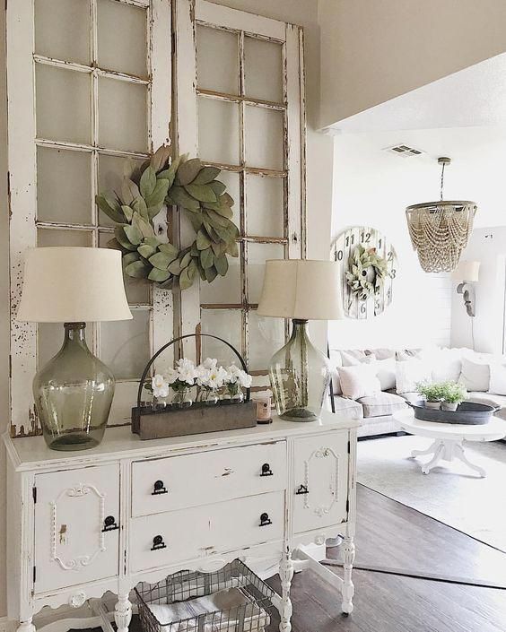 a cute shabby chic entryway with a chic sideboard, a wire basket, lamps, frames with a greenery wreath