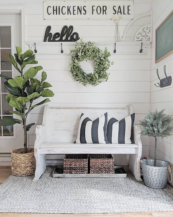 a farmhouse meets shabby chic entryway with signs, a white bench, baskets and potted greenery and trees