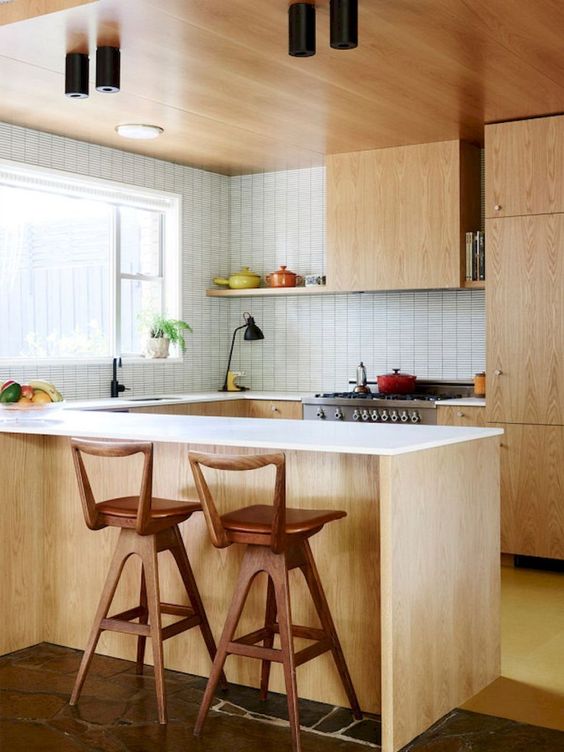 a light-colored mid-century modern kitchen with white countertops and tiled walls plus wooden stools
