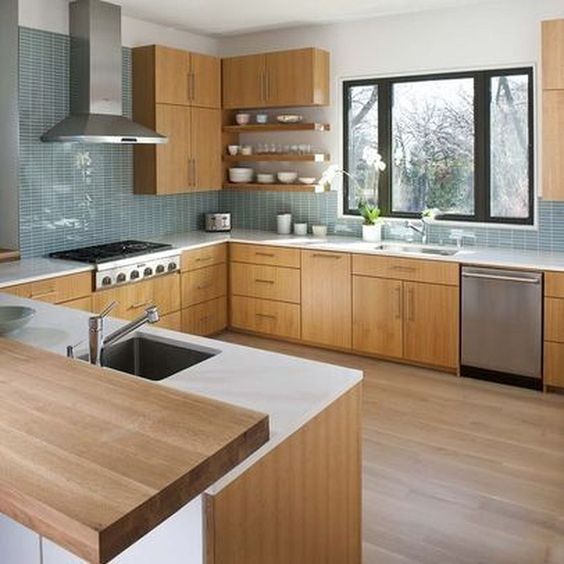 a light-colored wooden kitchen with white countertops, a blue tile backsplash and metal appliances