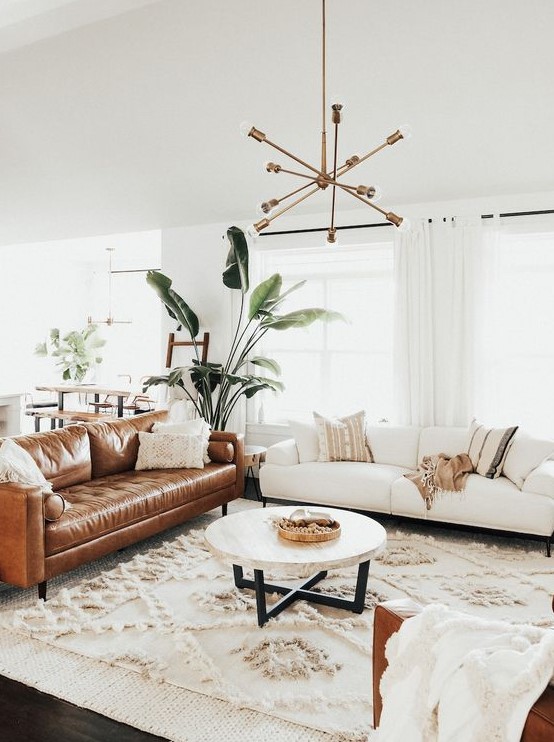 A light filled mid century modern living room with a creamy and amber leather sofa, a round table, a boho rug and a chic chandelier