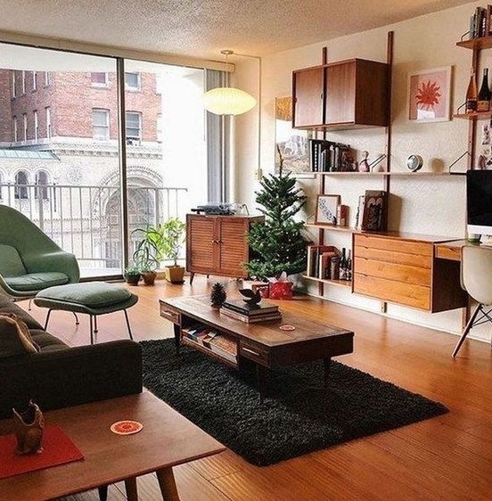 A lovely mid century modern living room with a green chair and a footrest, a black sofa, chic rich stained wooden furniture and potted plants