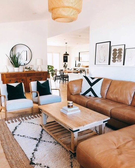 A mid century modern living room with a boho feel, an amber leather sofa, neutral chairs, a wooden coffee table, printed textiles