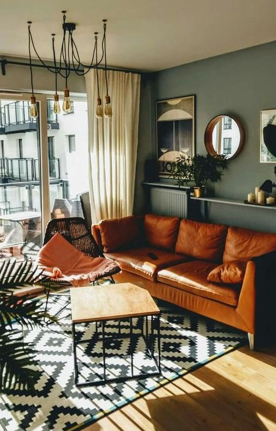 A mid century modern living room with grey walls, an amber leather sofa, a black woven chair, an open shelf with decor and mirrors