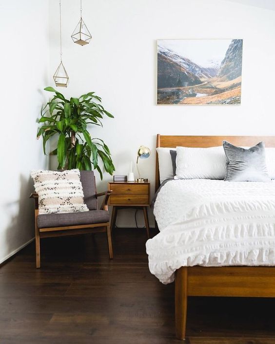A mid century modern meets boho bedroom with warm colored wooden furniture, an artwork, pendant lamps and a potted plant