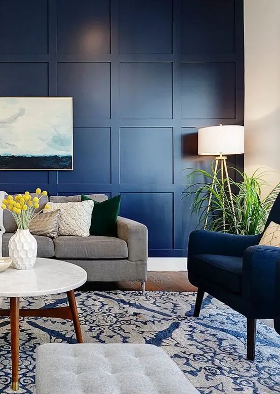 a modern living room with a navy panel wall, navy and grey furniture, potted greenery and a sea artwork