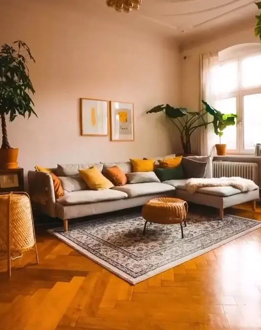 A modern warm toned living room with blush walls, a grey sectional, mustard and yellow pillows and potted plants
