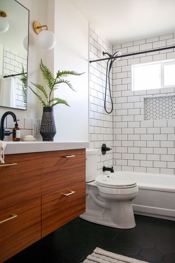 a monochromatic bathroom with white subway tiles and black hex ones, a wooden vanity and black fixtures for a bolder look