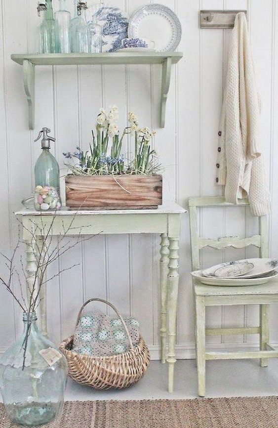 a neutral shabby chic entryway with pastel furniture - a chair, a console, a shelf, a box with blooms and a basket