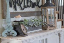 a pastel shabby chic entryway with a console table, a lantern with a pot, greenery in a box, a large chest, a candleholder and a sign with pompoms