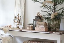 a shabby chic entryway with a long console table, a chest under it, a stool, a shutter, candelabras and candle lanterns