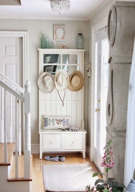 a shabby chic entryway with a storage unit with a seat, a rug, bottles and a whitewashed floor clock