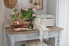 a shabby chic entryway with a wardrobe, a whitewashed console with a wooden top, a basket, potted blooms and art