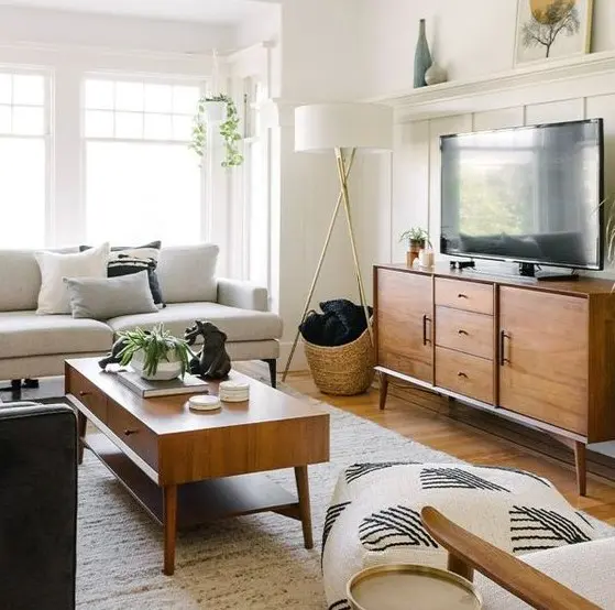 A simple mid century modern living room with a creamy sofa, a stained TV unit and coffee table, printed pillows and some greenery