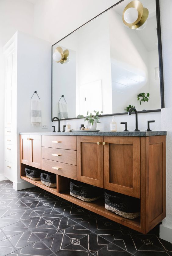 a stylish mid-century modern bathroom with black mosaic tiles, a large wooden vnaity with a stone countertop and touches of gold