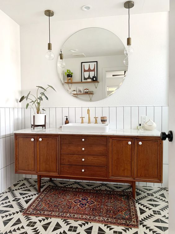 A stylish mid century modern bathroom with whiet skinny tiles, geo tiles on the floor, a boho rug, a wooden vanity and pendant lamps
