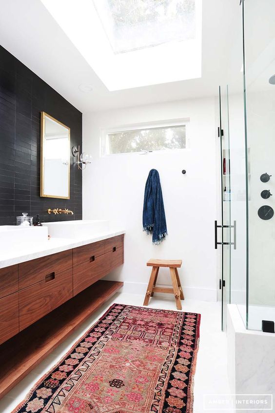 a stylish mid-century modern space with black and white skinny tiles, a redwood floating vanity, a boho rug and several skylights