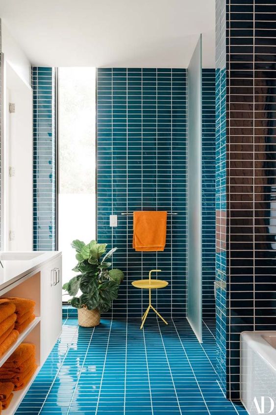 a vibrant mid-century modern bathroom clad with navy skinny tiles, a white flaoting vanity and touches of orange