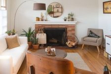 a welcoming mid-century modern living room with a creamy sofa, a tan and an maber chair, a coffee table, a fireplace clad with brick and a cool floor lamp