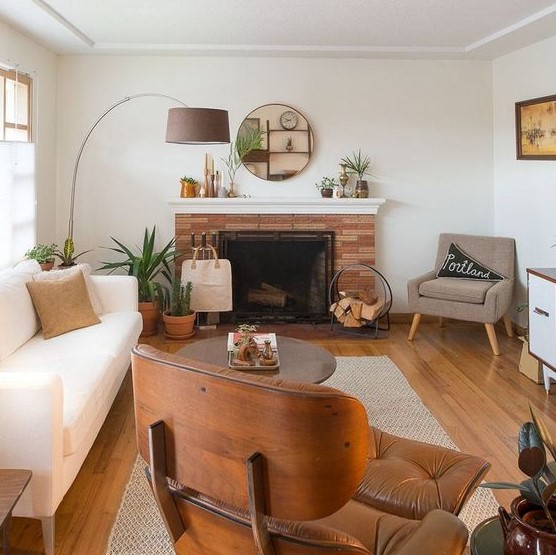A welcoming mid century modern living room with a creamy sofa, a tan and an maber chair, a coffee table, a fireplace clad with brick and a cool floor lamp