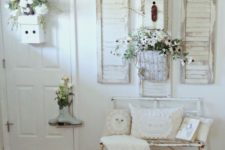 a white shabby chic entry with a metal bench, potted blooms and greenery, shutters on the wall and signs