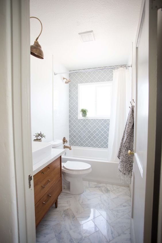 An airy mid century modern bathroom with grey Moroccan tiles, white marble ones, a wooden vanity and touches of brass