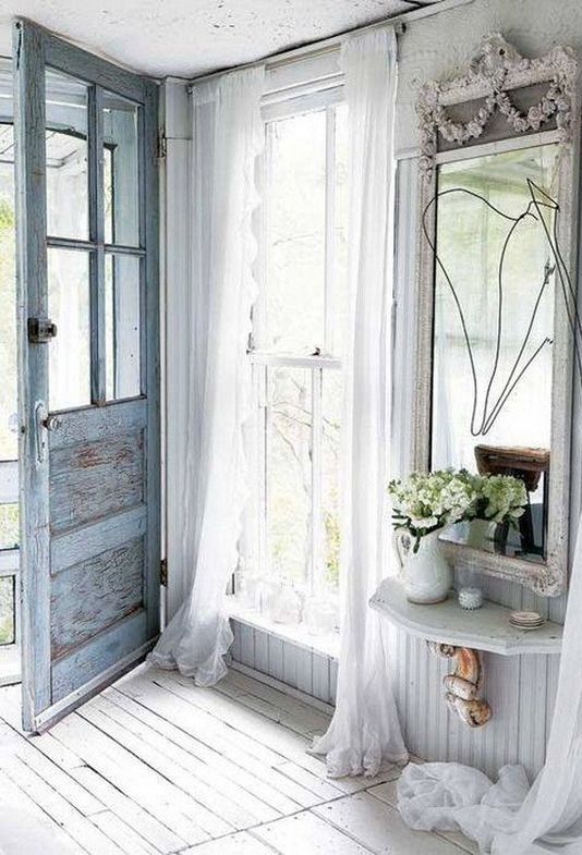 an airy shabby chic entryway with a blue door, a large mirror, a floatign shelf, tulle curtains and some blooms