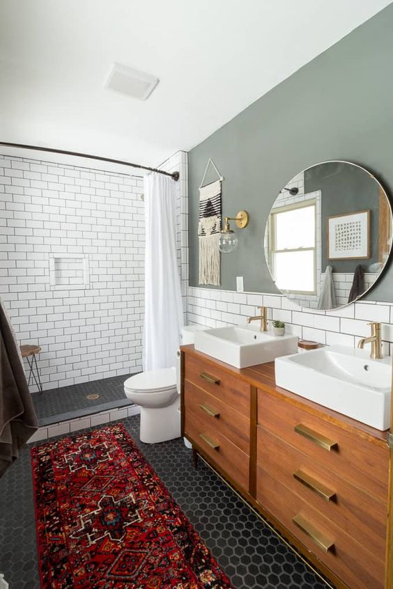 An amazing mid century modern bathroom with white subway tiles and black hex ones, a bright rug and a wooden vanity with gold touches